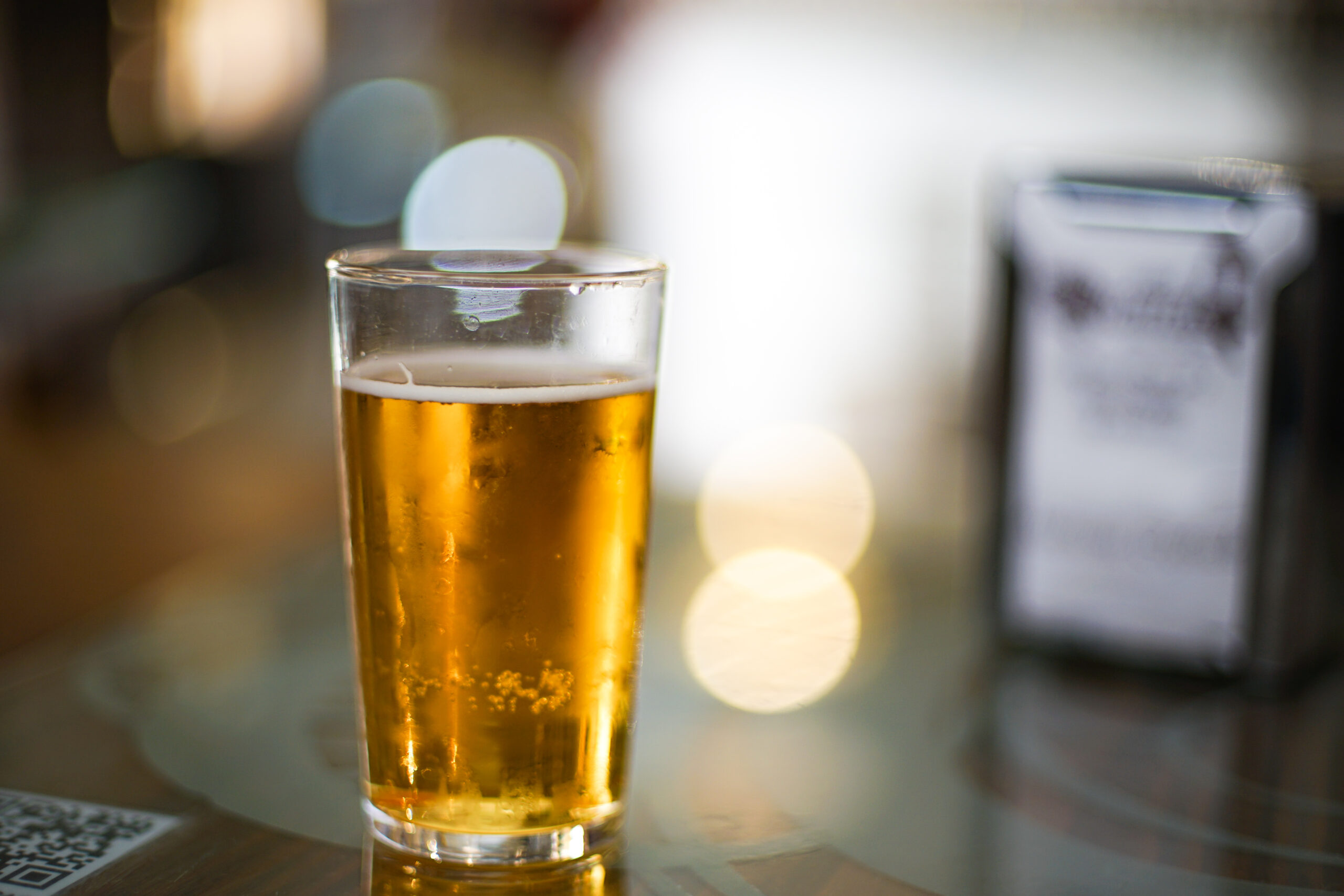 A glass of pale golden helles lager with a thin white head on a bar table