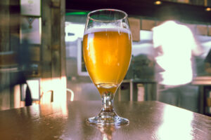 A tulip glass of hazy golden-orange pale ale with a white head in a sunlit taproom